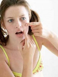 A teenage girl is squeezing a pimple on her cheek.